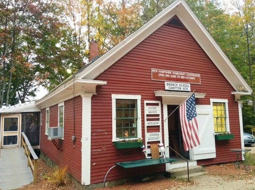 Red wooden building with a white roof, featuring an American flag and a sign for Brackett School in Campton, NH.