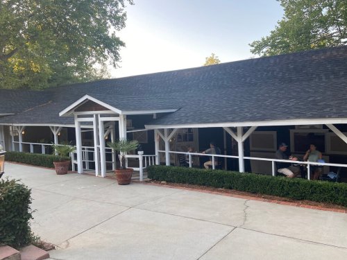 A white building with a sloped roof, featuring outdoor seating and greenery along the pathway.