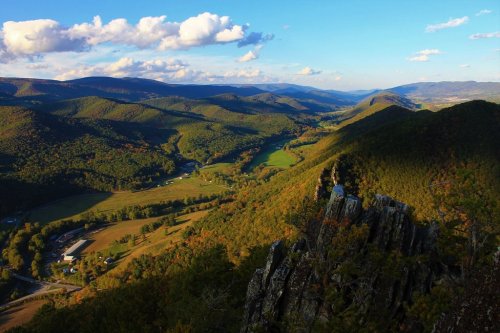 A panoramic view of rolling green hills and valleys under a blue sky with scattered clouds.