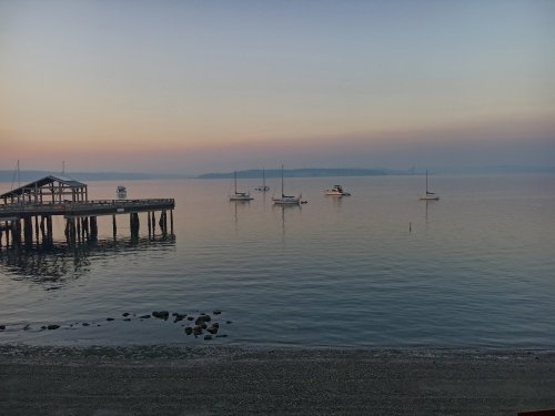 A serene waterfront scene at dusk, featuring a pier and several sailboats on calm waters with a soft gradient sky.