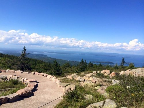 Scenic view from a mountain overlooking a lake and distant islands, with blue skies and scattered clouds.