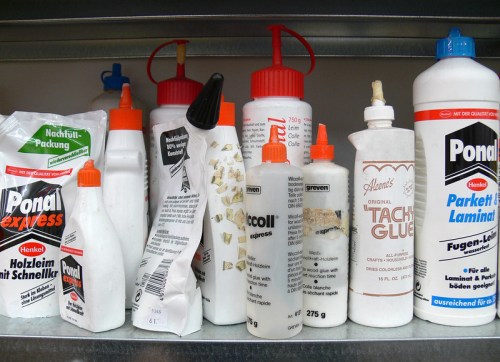 A shelf filled with various bottles of glue, including Ponal and other brands, in different shapes and sizes.