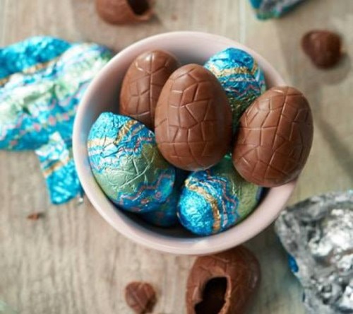 A bowl filled with chocolate eggs, some wrapped in colorful foil, on a wooden surface.