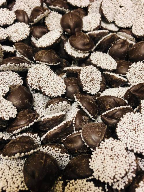A close-up of dark chocolate discs coated with tiny white sprinkles, creating a textured, visually appealing surface.