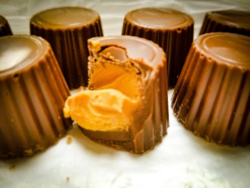 A close-up of chocolate cups, one with a bite taken out, revealing creamy peanut butter filling inside.