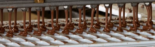 Chocolate being poured into molds on a production line, creating evenly shaped chocolate pieces.