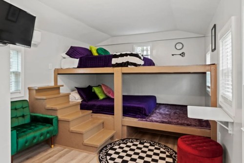A cozy room with a bunk bed, colorful pillows, a green chair, and a checkered rug, featuring bright natural light.