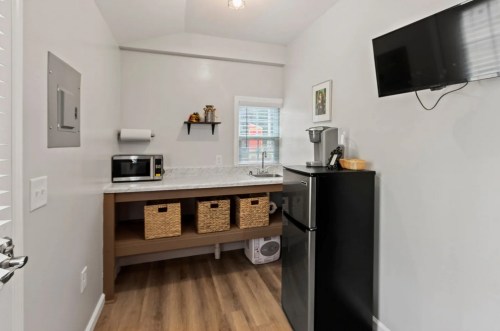 A modern kitchen with a microwave, sink, black fridge, and storage baskets on a wooden counter.