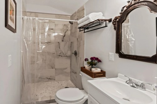 A modern bathroom featuring a marble shower, white sink, decorative mirror, and neatly arranged towels and flowers.