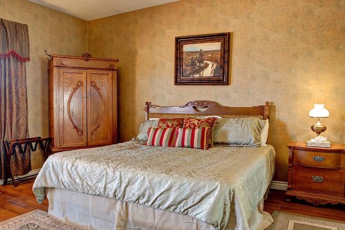 Cozy bedroom featuring a wooden bed, decorative pillows, an armoire, and a bedside lamp against a textured wall.