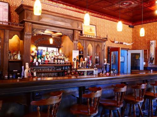 A vintage bar with wooden decor, shelves of liquor bottles, and empty stools under warm pendant lights.