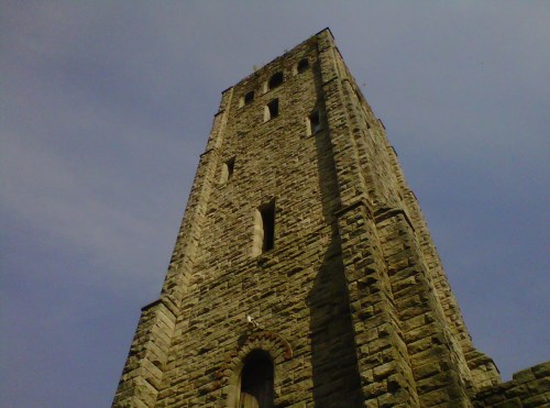 A tall stone tower against a blue sky, showcasing its textured surface and several narrow windows.