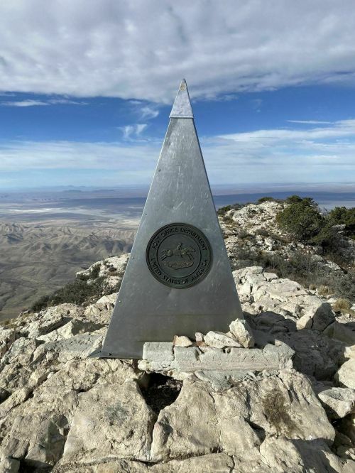 A tall, silver pyramid monument on a rocky mountain peak, with a seal at its base and a vast landscape in the background.