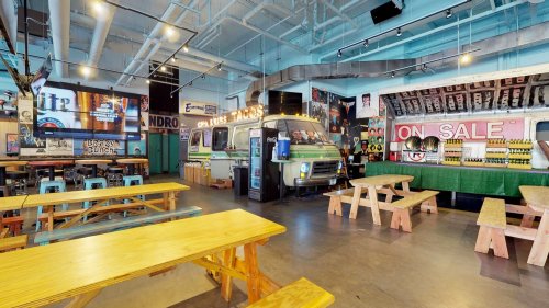 A vibrant indoor space featuring wooden tables, a vintage food truck, and colorful decor with posters and bar seating.