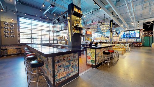A vibrant bar area with colorful decor, high stools, and a large window, featuring a modern, industrial design.