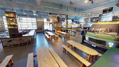 A spacious bar with wooden tables, a large counter, and a colorful food truck mural on the wall. Bright and modern interior.
