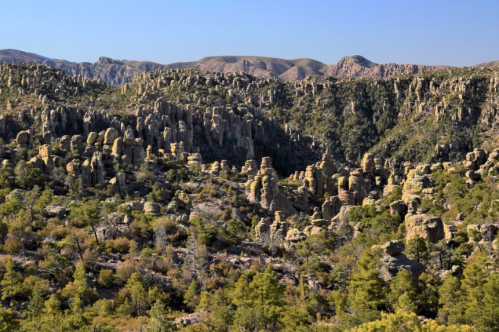 A rugged landscape featuring towering rock formations and lush greenery under a clear blue sky.