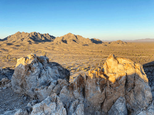 A panoramic view of rugged mountains and a vast desert landscape under a clear blue sky.