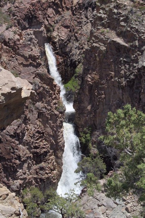 A waterfall cascading between rocky cliffs, surrounded by sparse greenery in a rugged landscape.