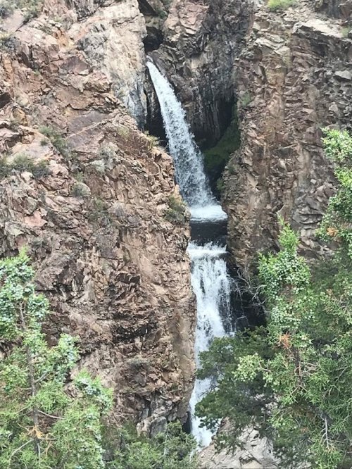 A waterfall cascading between rocky cliffs, surrounded by lush greenery.