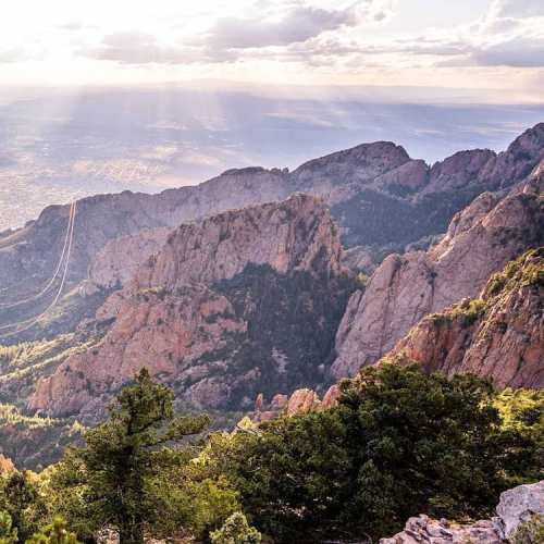 A scenic view of rugged mountains with sunlight streaming through clouds, surrounded by lush greenery.