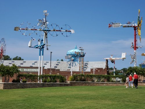 Colorful wind sculptures and whimsical structures in a park under a clear blue sky, with people walking nearby.