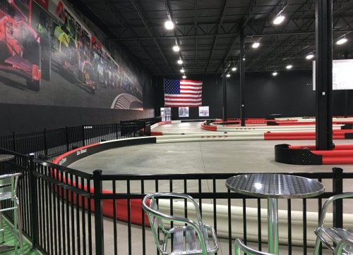 Indoor go-kart track with red and white barriers, a large mural, and an American flag hanging on the wall.