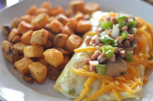 A plate of cheesy omelette topped with green peppers and diced ham, served with golden-brown roasted potatoes.