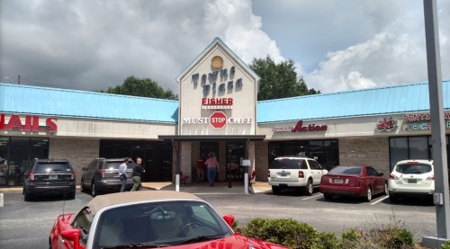 A storefront with a blue roof featuring "Must Stop Cafe" and various shops, with cars parked outside.