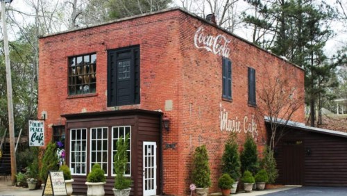 A charming brick café with large windows and greenery, featuring a sign that reads "Café" and "Nature Café."