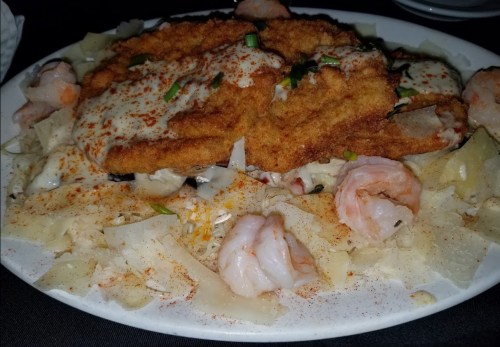 A plate of fried fish topped with creamy sauce, shrimp, and garnished with green onions, served over a bed of noodles.