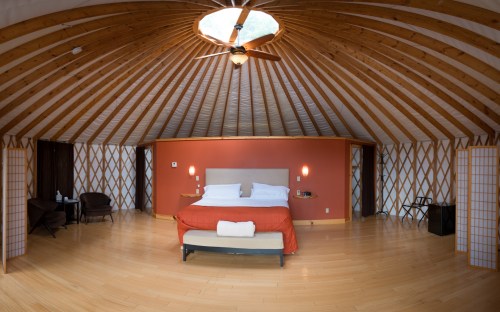 Cozy yurt interior featuring a large bed, wooden ceiling, and warm decor with seating areas.