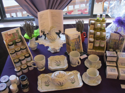A display of lavender-themed products, including tea sets, oils, and soaps, arranged on a purple tablecloth.