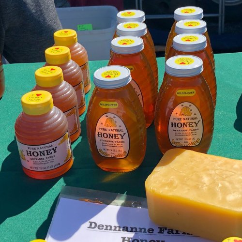 Bottles of honey and a block of beeswax displayed on a green table at a market.