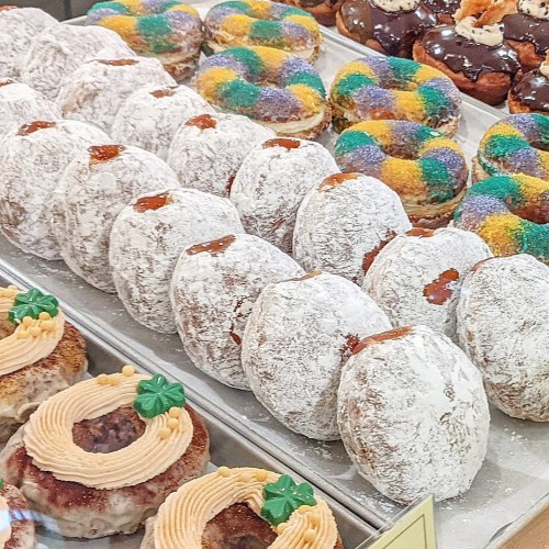 A display of assorted donuts, including powdered, glazed, and festive Mardi Gras-themed varieties.