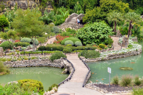 A serene garden with lush greenery, winding paths, and a pond filled with koi fish, surrounded by vibrant flowers.