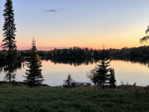 A serene lake at sunset, surrounded by trees, reflecting colorful skies and calm waters.