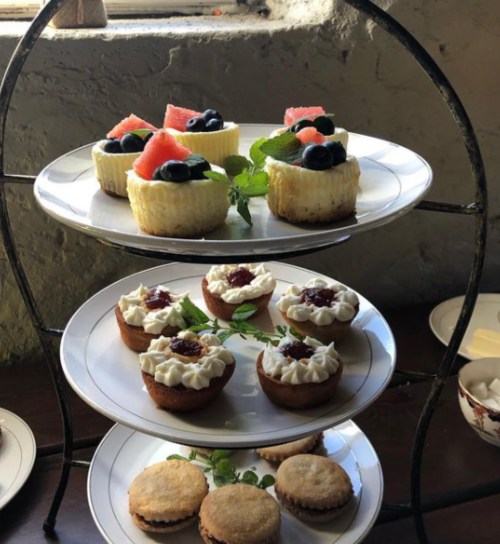 A tiered dessert stand featuring mini cheesecakes, fruit, and cream-filled pastries, garnished with mint leaves.