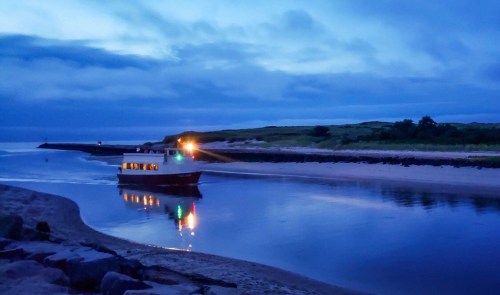 A boat navigates a calm waterway at dusk, with soft blue hues and reflections on the water.