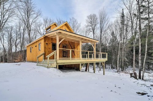 A wooden cabin with a porch, surrounded by snow-covered trees in a winter landscape.