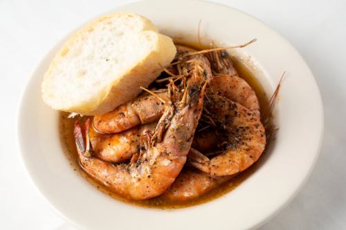 A bowl of seasoned shrimp in sauce, served with a slice of bread on the side.
