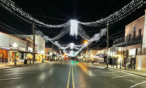 A quiet street at night adorned with festive lights and decorations, showcasing shops on either side.
