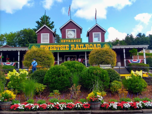 Entrance to Tweetsie Railroad, featuring a colorful sign, flowers, and a clock tower, with visitors in front.