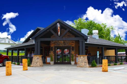 A rustic restaurant with a stone facade and a black roof, surrounded by greenery and a blue sky with clouds.