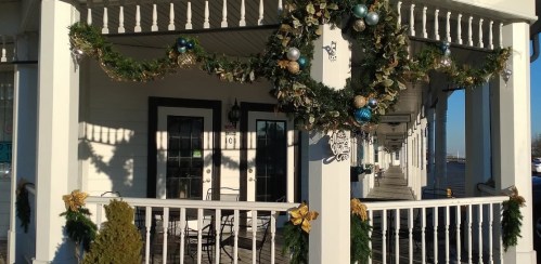 A decorated porch with garlands, wreaths, and ornaments, featuring chairs and a sunny outdoor view.