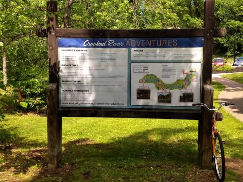 Sign for Crooked River Adventures detailing activities, pricing, and a map, with a bike parked nearby.