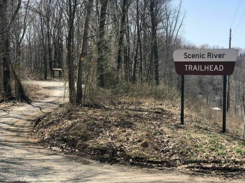 A sign for the Scenic River Trailhead at a wooded path, with bare trees and a clear sky in the background.