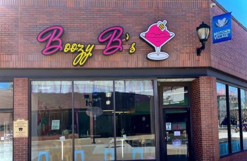 Exterior of Boozy B's, a colorful bar with a cocktail logo, located in Midtown Village. Bright signage and large windows.