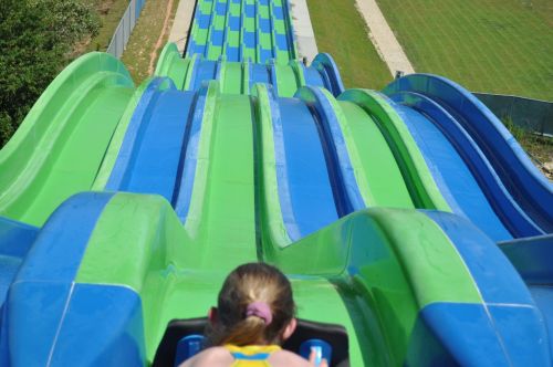 A view from the top of a colorful water slide, showing the winding path down and a person preparing to slide.