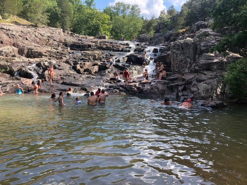 People swimming and relaxing in a natural pool surrounded by rocky terrain and lush greenery.